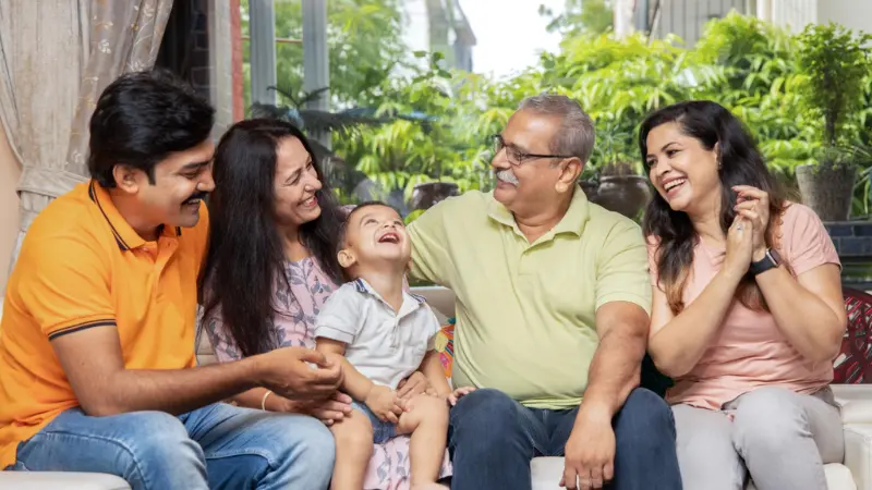 घर में बैठकर मजेदार बातें करते और हँसते भारतीय परिवार के सदस्य